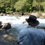 Artisan de la marque Obscura Sancta en montagne, près d'une rivière, de dos