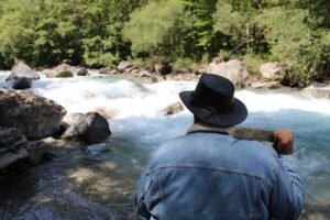 Artisan de la marque Obscura Sancta en montagne, près d'une rivière, de dos